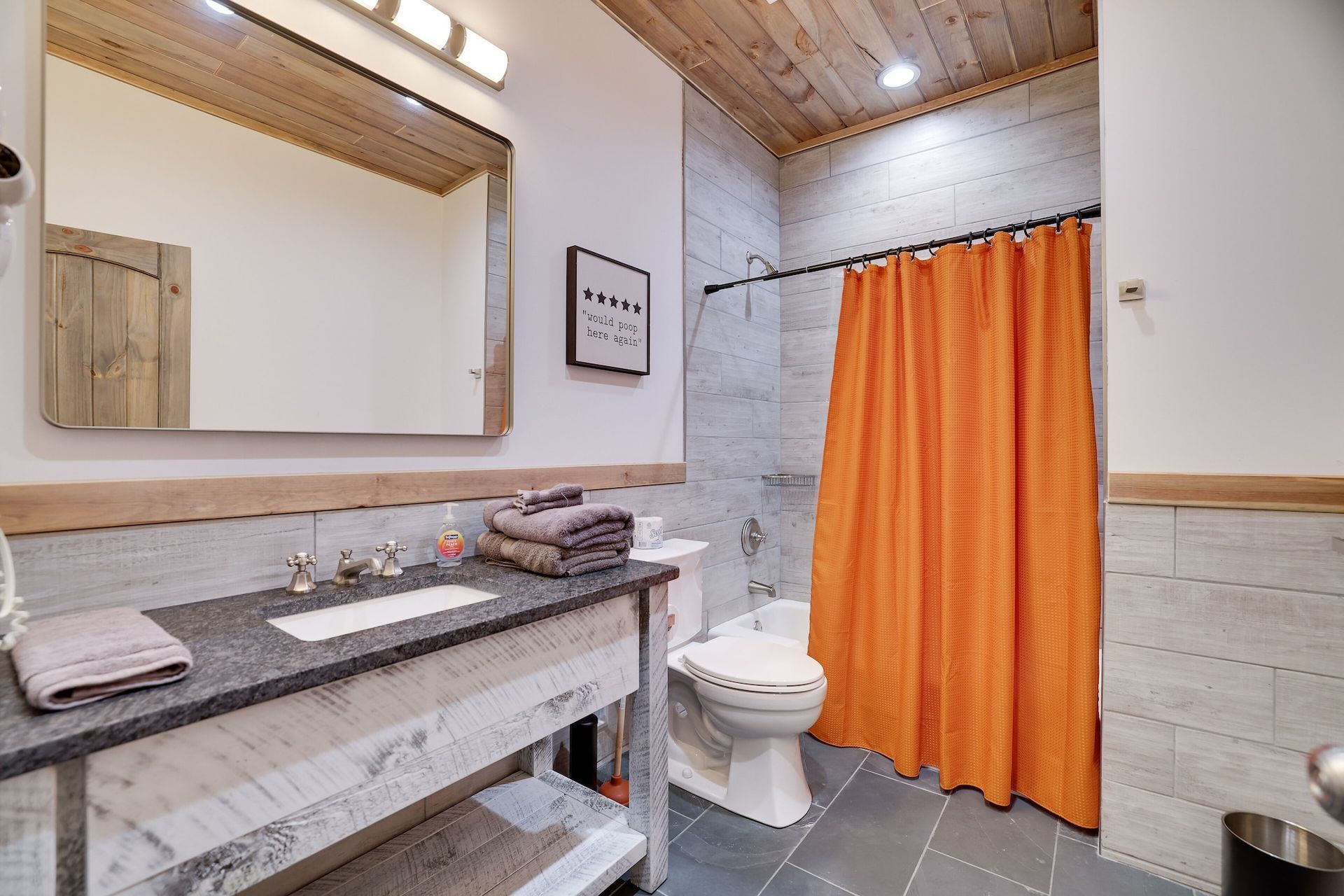 A bathroom with a toilet , sink , mirror and orange shower curtain.