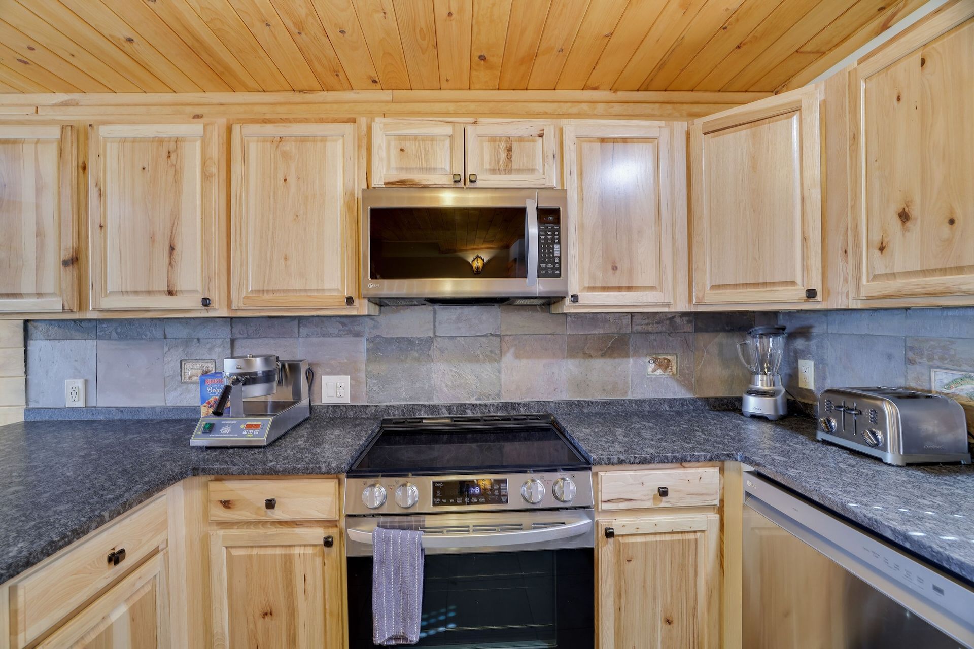 A kitchen with stainless steel appliances , granite counter tops , wooden cabinets and a stove.