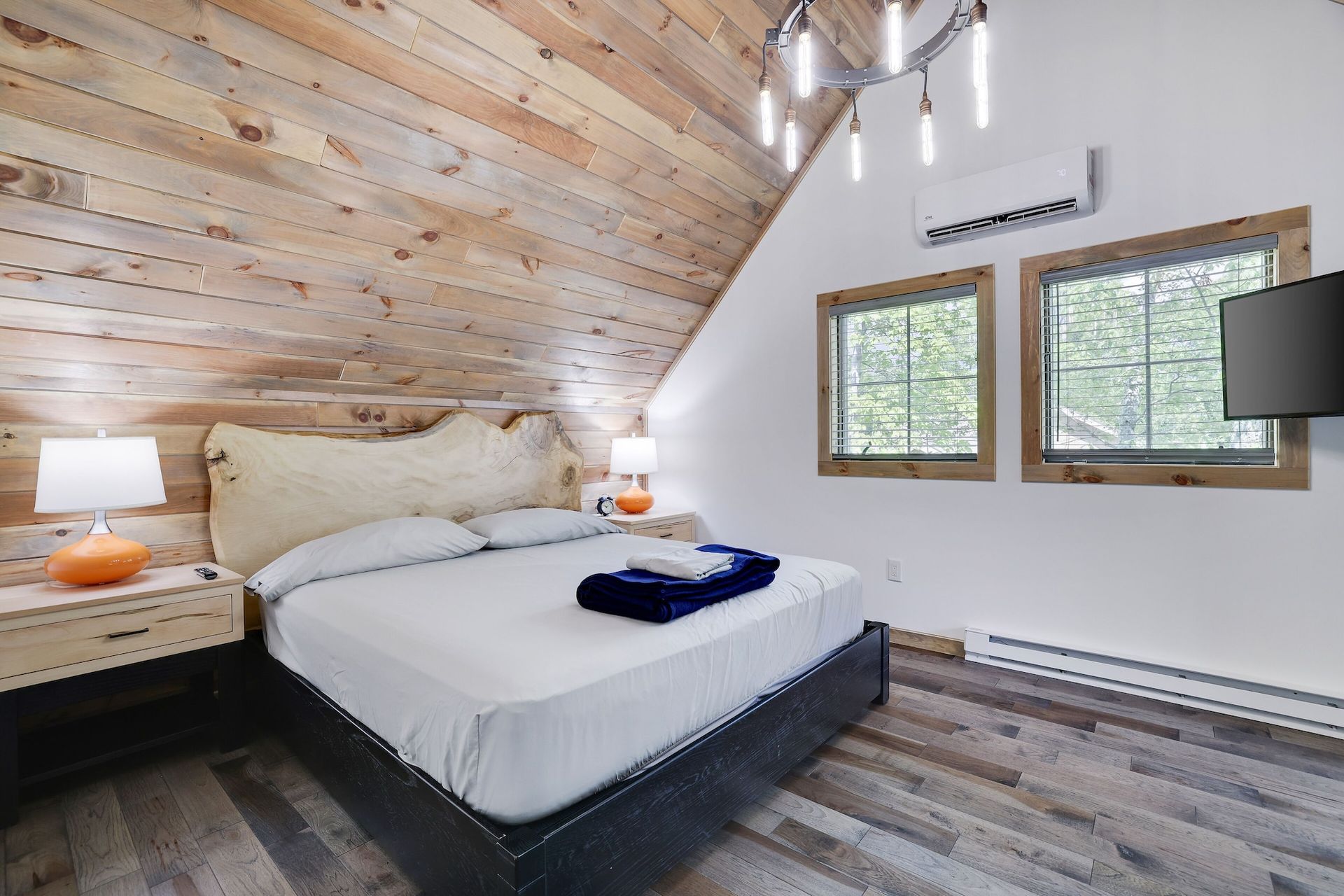 A bedroom with a king size bed , two nightstands , two windows and a flat screen tv.