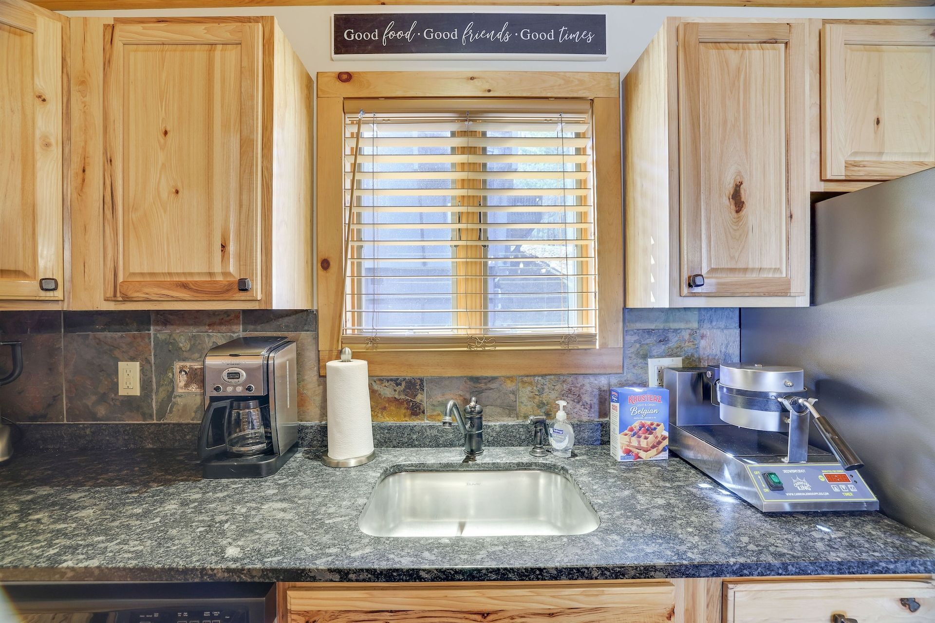 A kitchen with a sink , mixer , coffee maker , and a window.