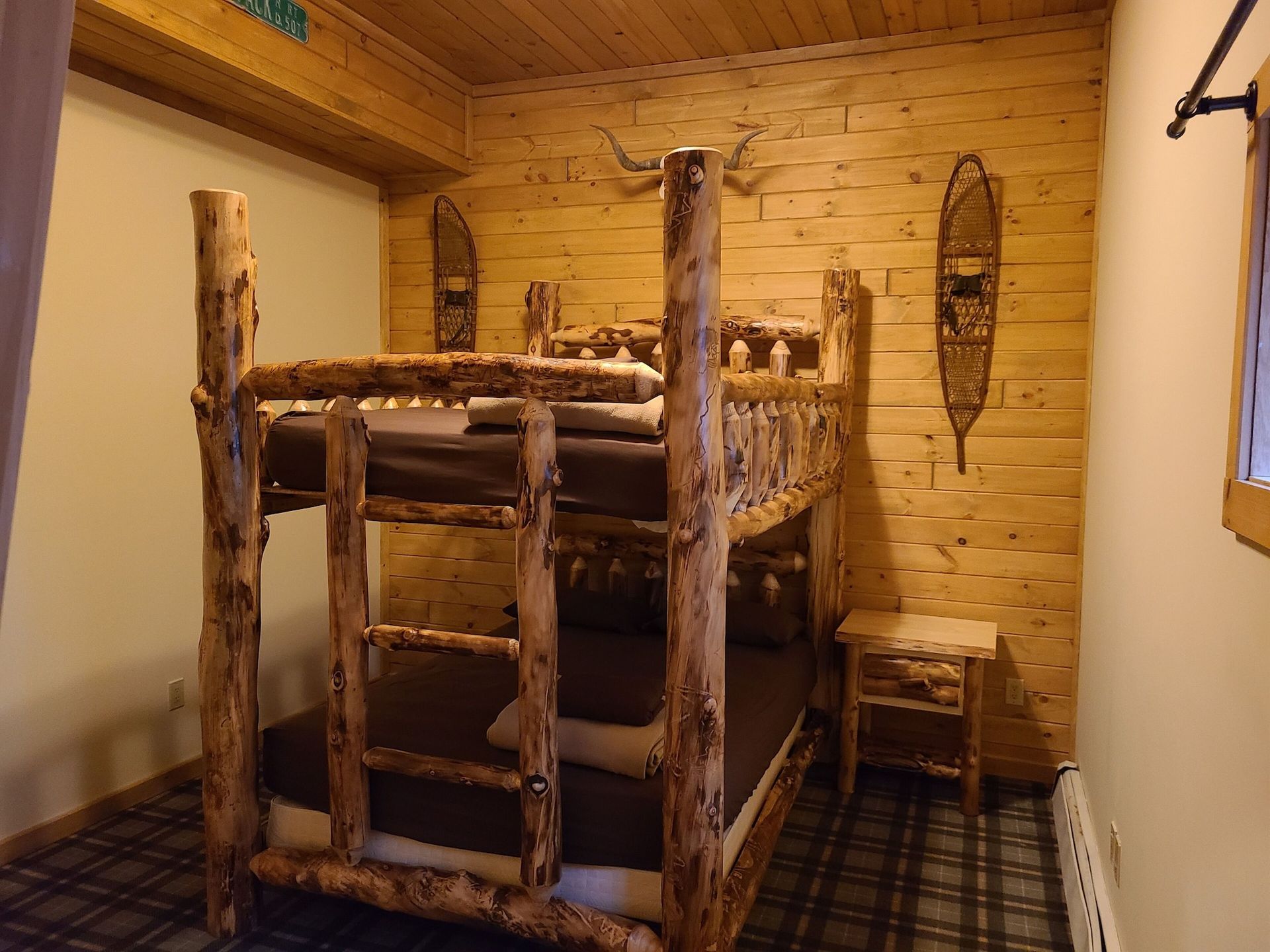 A bunk bed made of logs is in a room with a wooden wall.