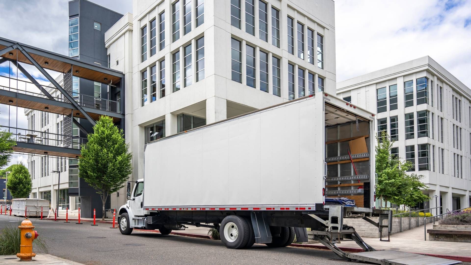 White moving truck backed up to modern office buildings.