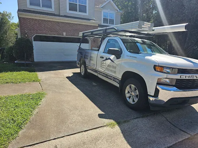 White Chevy truck with a ladder rack parked in front of a house with a closed garage door.