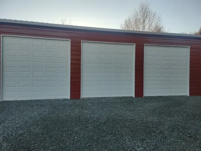 Three white garage doors on a red building, set against a gravel surface.