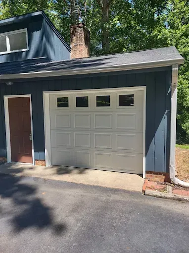 White garage door on a blue house with a brown door to the side. Paved driveway.