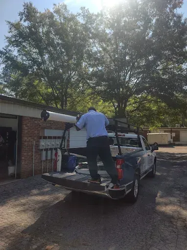 Man loading long white equipment onto a truck bed, under bright sun.