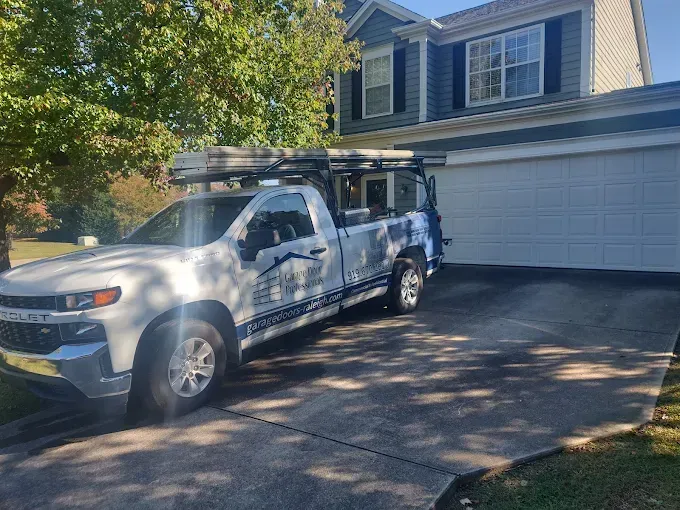 White Chevy truck parked in driveway in front of a two-story house with a closed garage door.