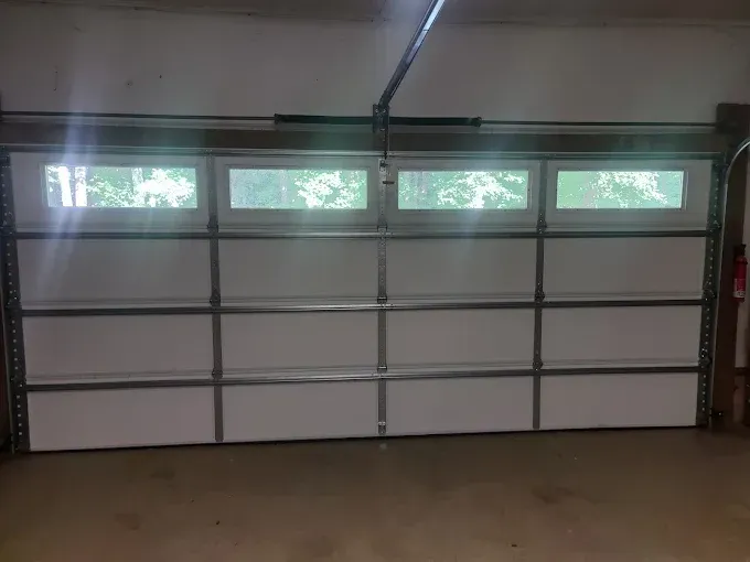 White garage door with four windows, facing outside; gray metal frame.