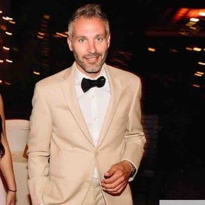 Man with glasses, bald head, and beard smiles, wearing a brown jacket over a yellow and blue plaid shirt.