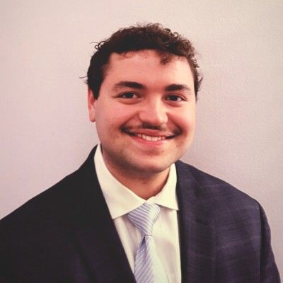 Woman smiling, holding pen, at a table, facing someone out of frame. Sunlight-filled room.