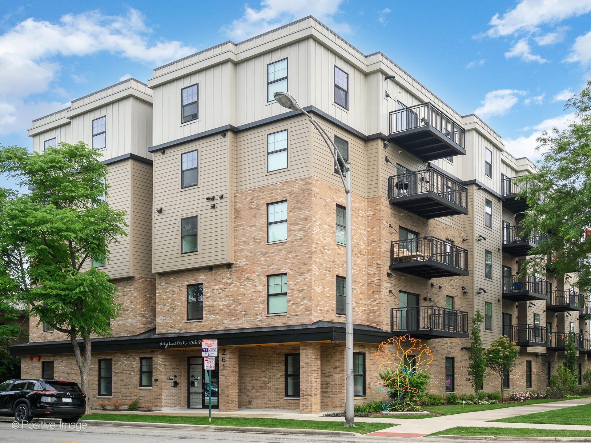 Multi-story brick apartment building with balconies, trees, and street lamp.