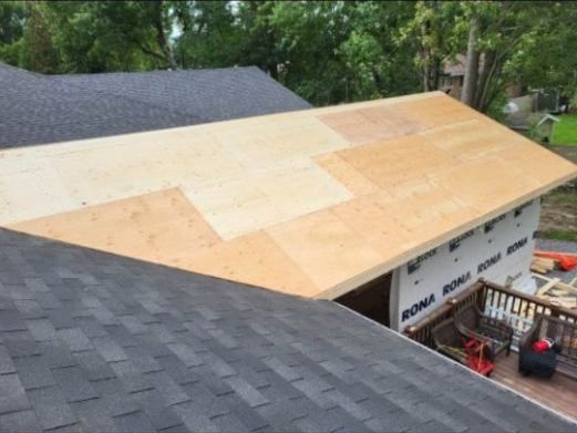 Vue aérienne du toit d'une maison, montrant une nouvelle section de revêtement en contreplaqué clair adjacente aux bardeaux existants.