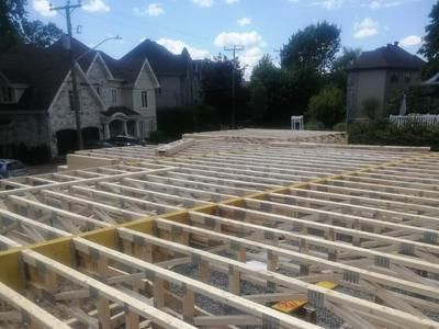 Une grande structure en bois est en cours de construction devant une maison.