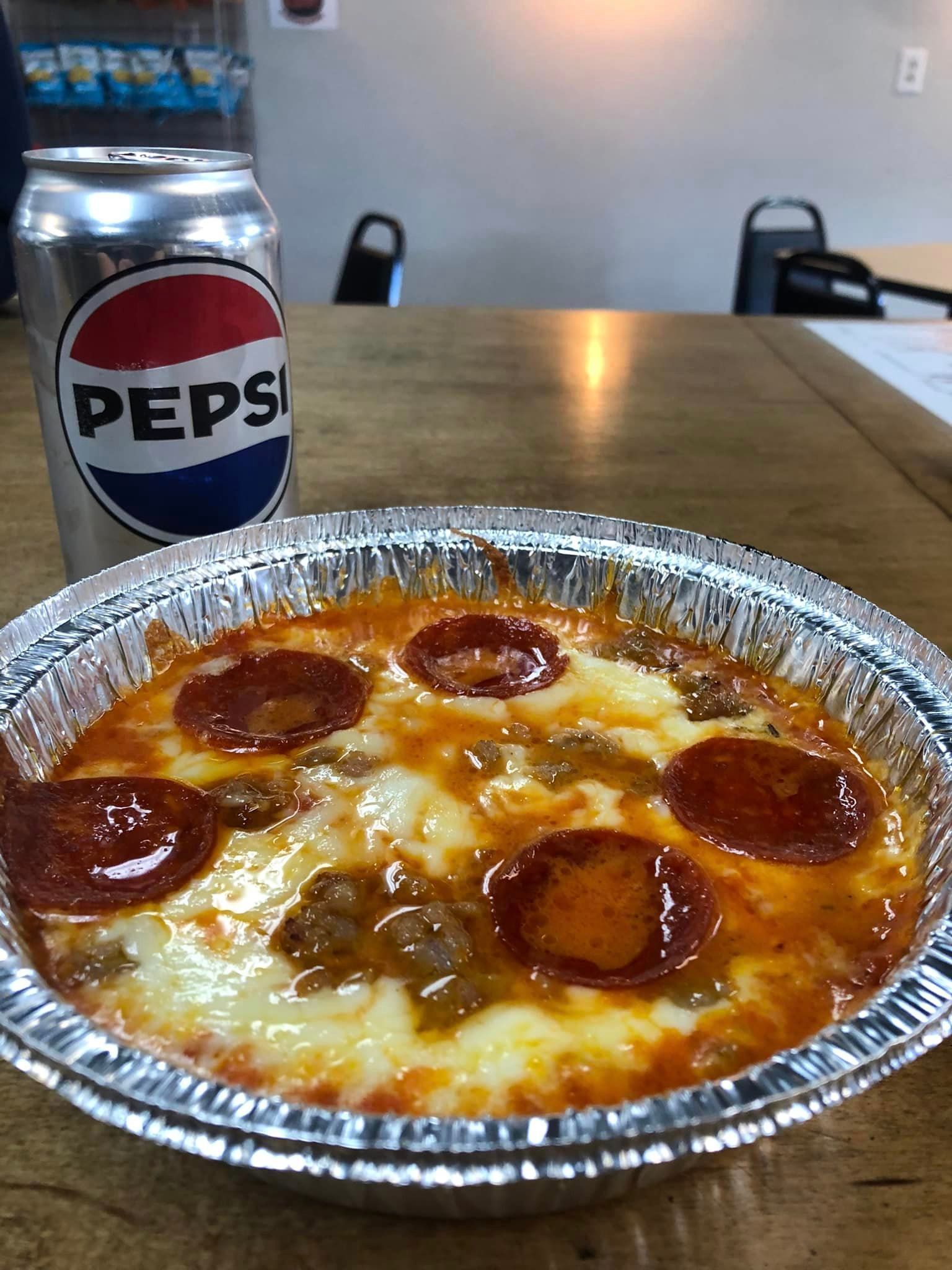 A pizza in a tin foil pan next to a can of pepsi.