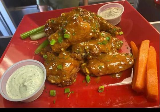 A red plate topped with chicken wings , carrots and ranch dressing.