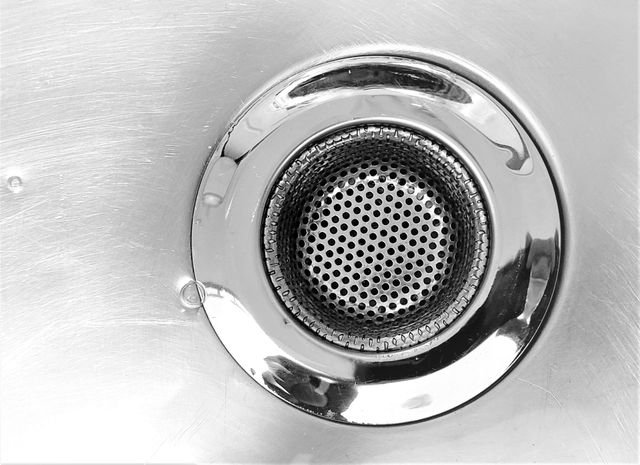 Square shower drain with concentric circle design, centered on white tiled floor.