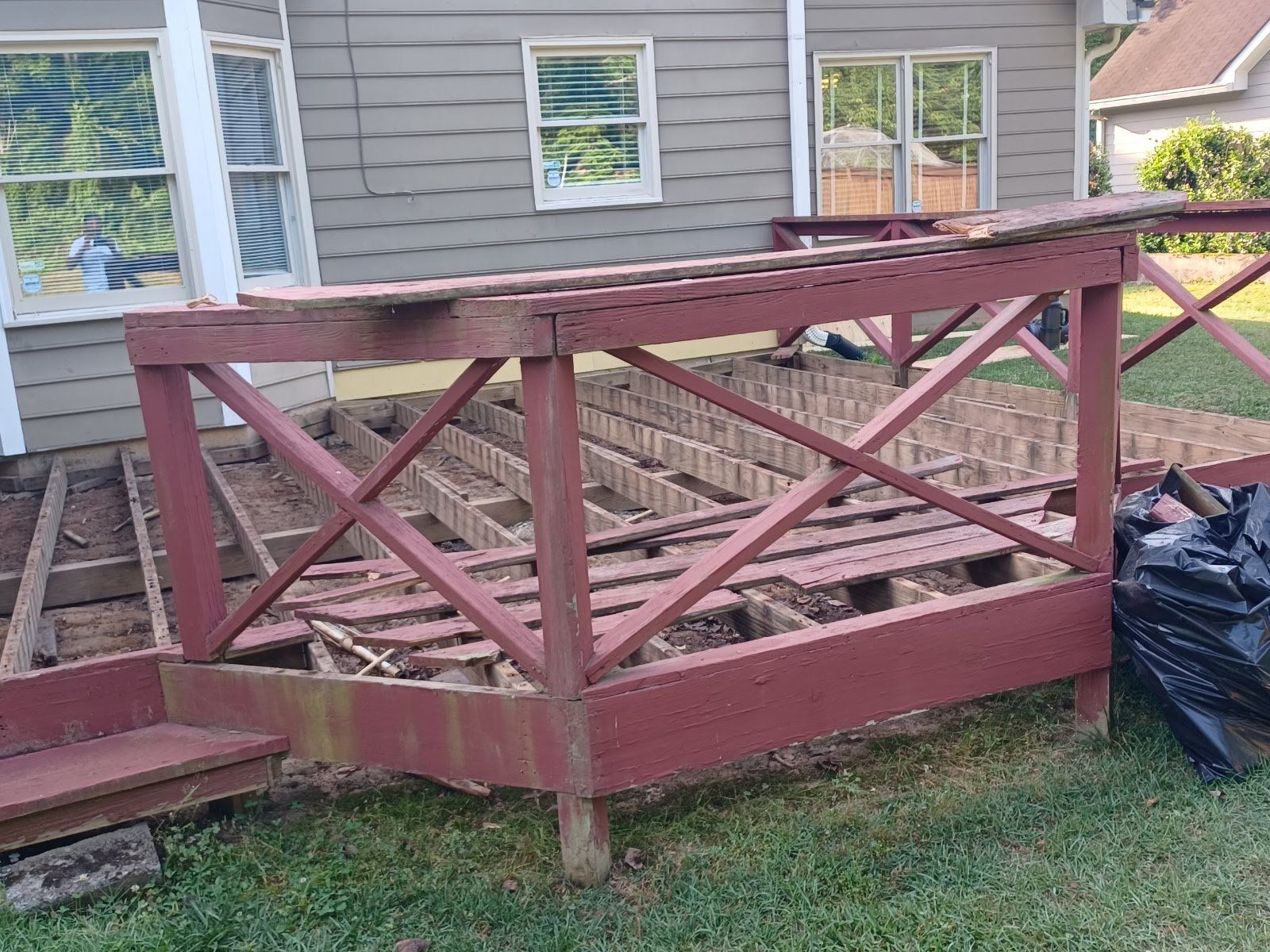 Partially dismantled wooden deck next to a house with missing planks and red railing.