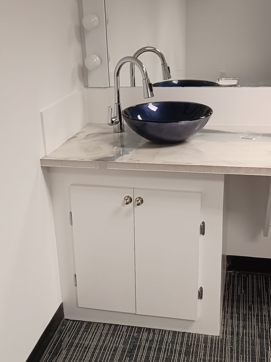 Vanity with a blue bowl sink, chrome faucet, white cabinet, and mirror in a white room.