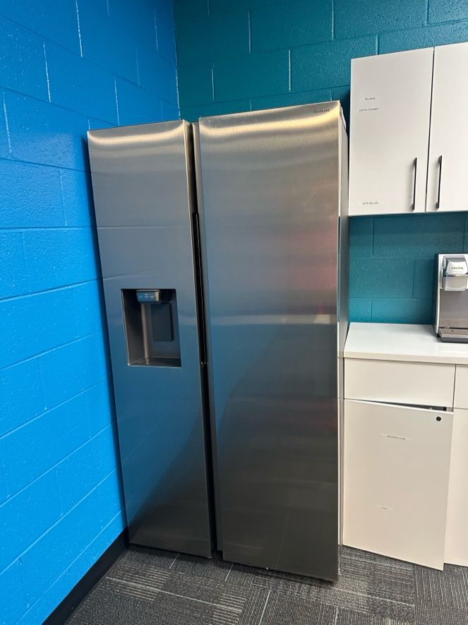 Stainless steel side-by-side refrigerator in a corner with blue wall. White cabinets and a counter are to the right.