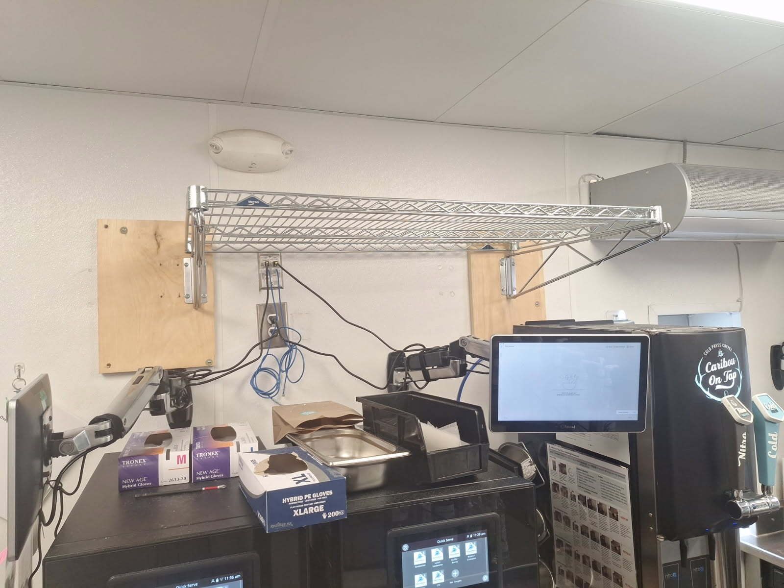 Cash register station with a shelf, monitor, wires, and boxes on a counter.