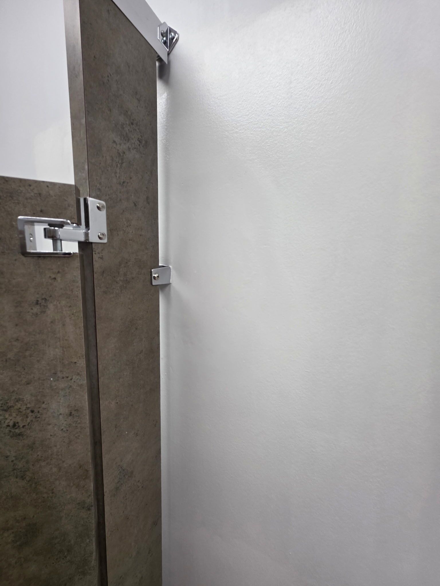 Bathroom stall door, metal hinges, attached to brown textured wall, white wall.