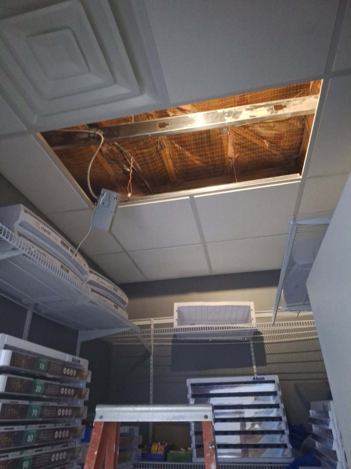 Ceiling tile removed exposing air duct and wires; a ladder is visible in the room.