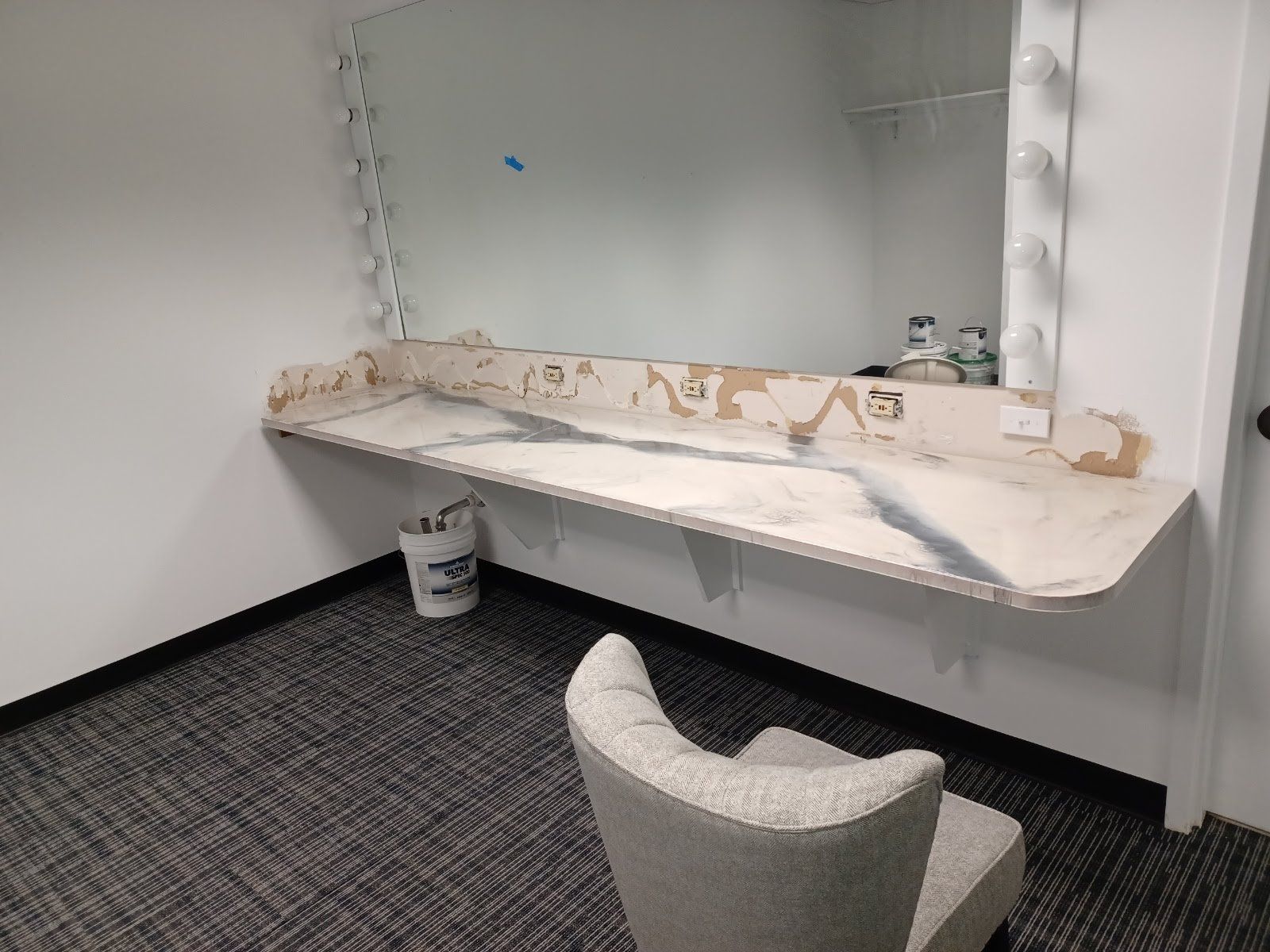 Makeup vanity with large mirror, peeling countertop, and chair in a room.