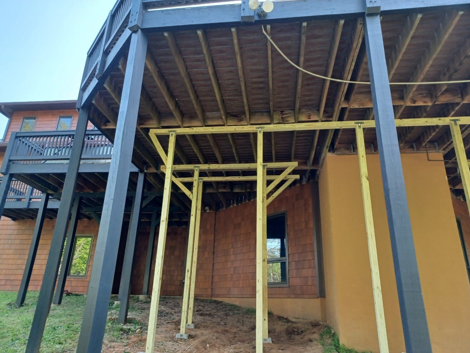 Wooden deck supported by yellow scaffolding, built over a brick and stucco structure.