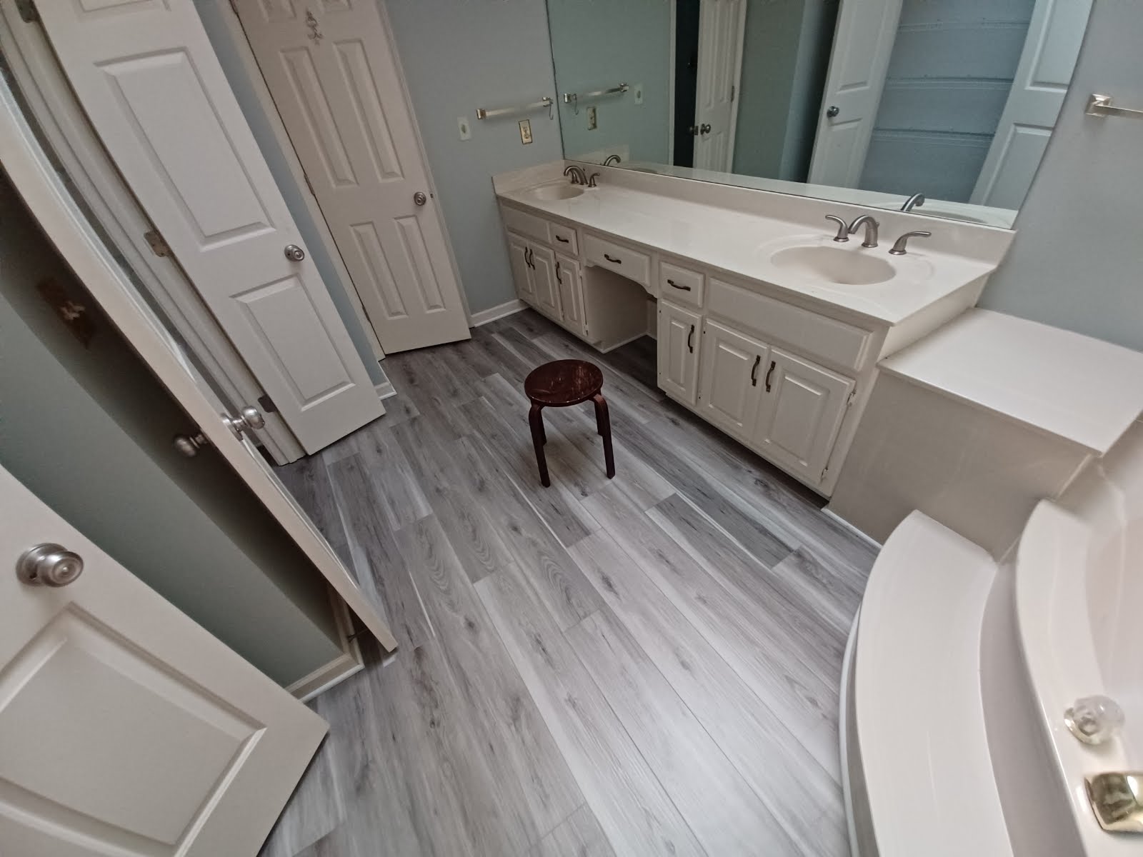Bathroom with white cabinets, gray wood-look flooring, and a small wooden stool.