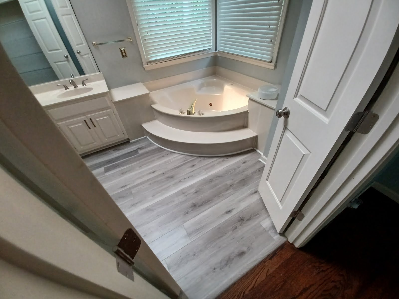 Bathroom with a white vanity, a corner jacuzzi tub, and light gray wood-look flooring.