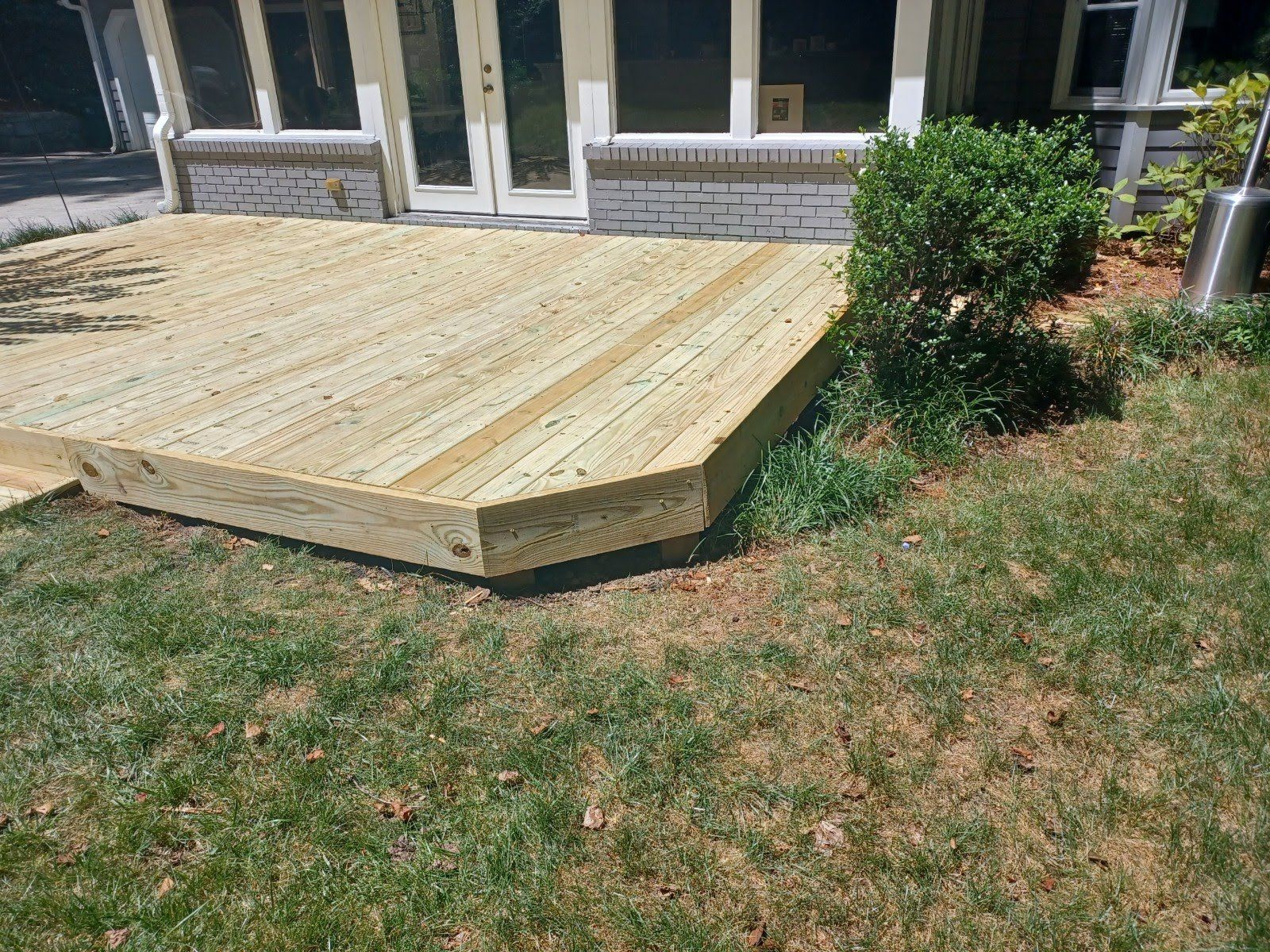 Wooden deck adjacent to a house with a grass yard.