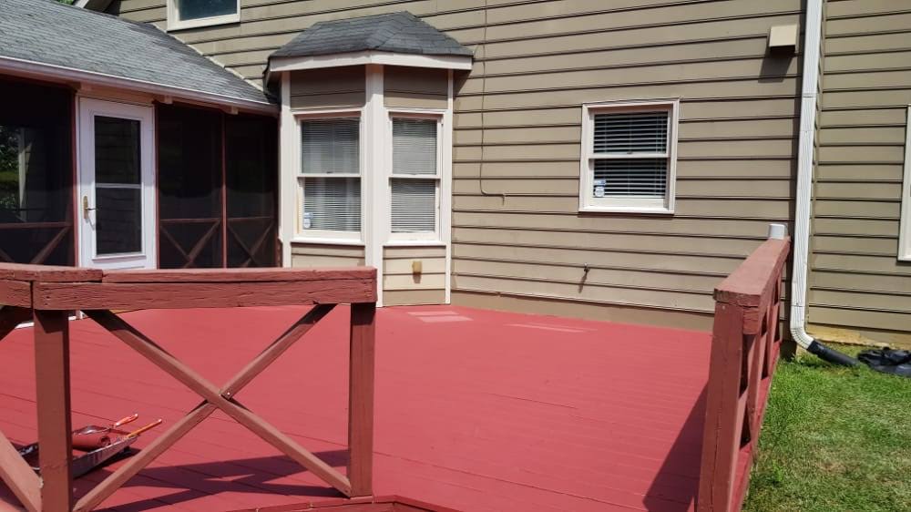 Red deck outside a tan house with windows and a screened-in door, sunny day.