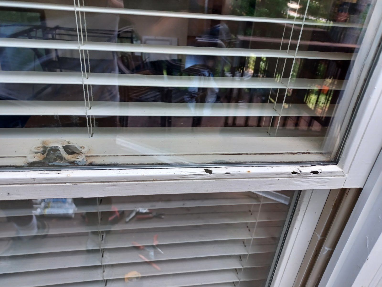 Close-up of a window with blinds partially open. White frame and a blurry reflection.
