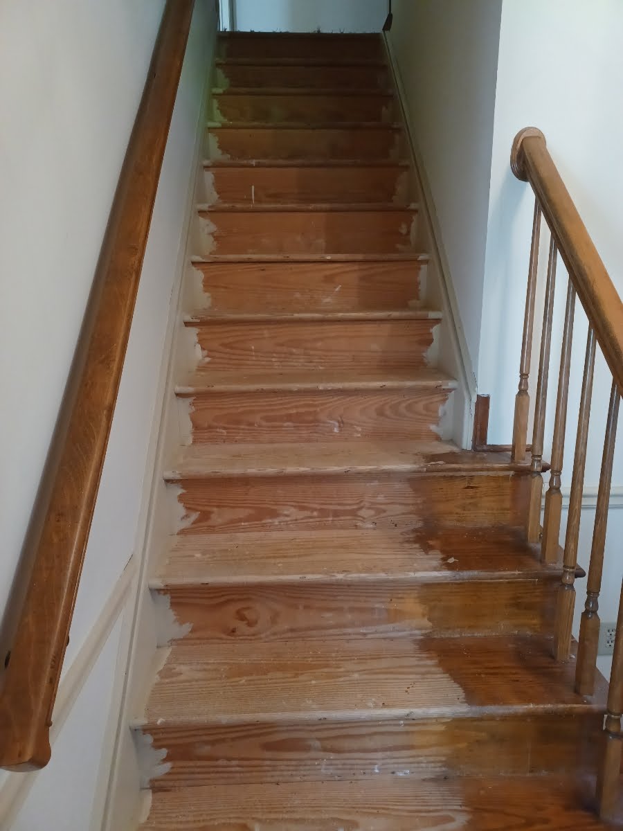 Wooden staircase with worn steps, two handrails, and white walls.