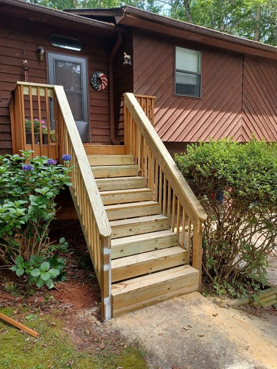 Wooden staircase leading up to a brown house with a door, surrounded by greenery.