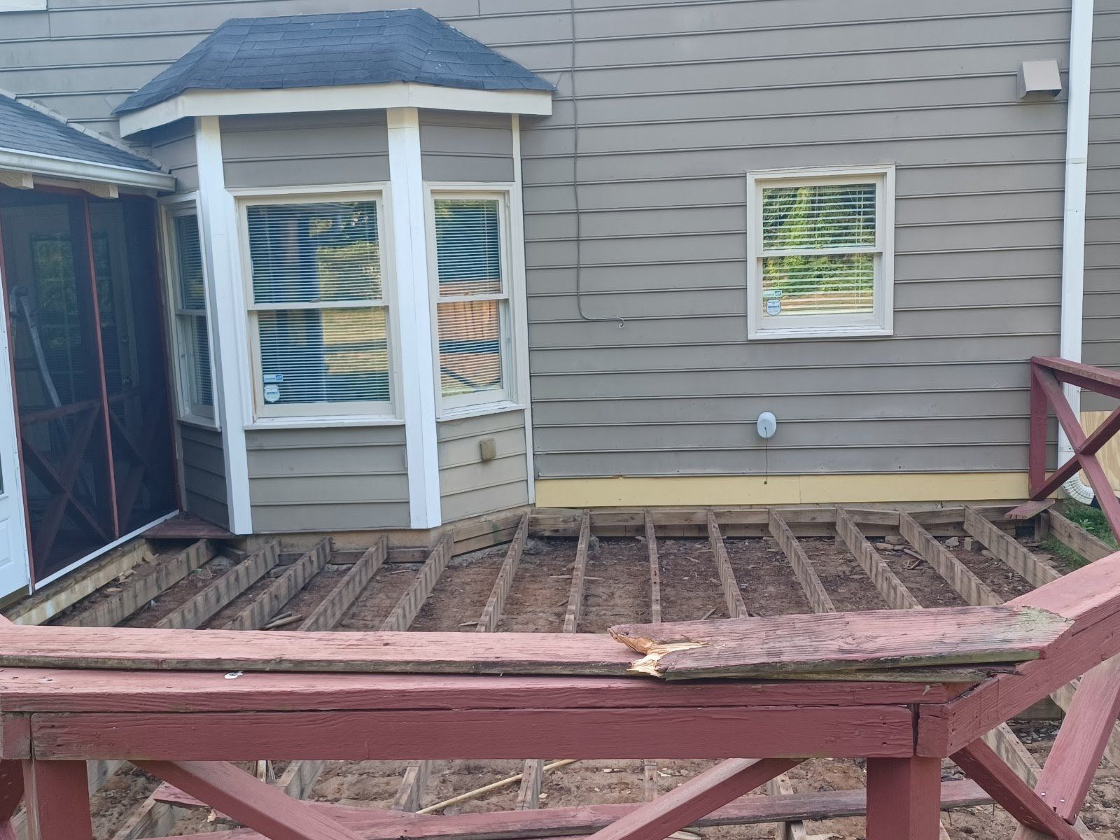 Deck under construction next to a house with bay window and a red railing.