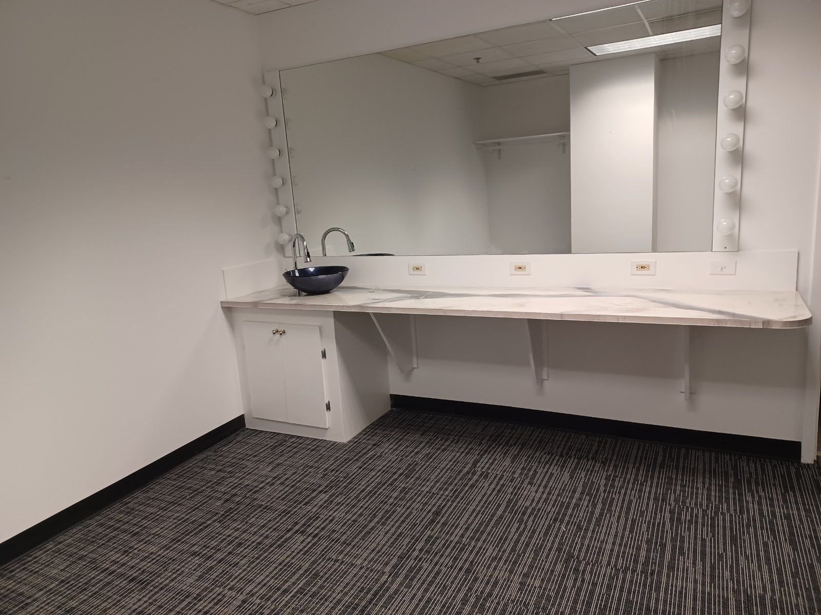 Vanity area with large mirror, countertop, sink, and cabinet in a room with patterned carpet.