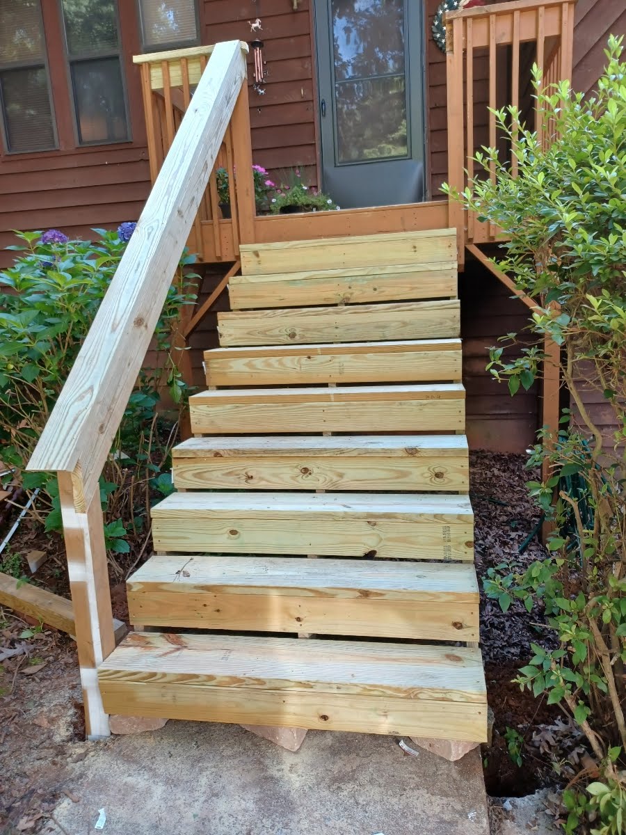 Wooden outdoor staircase leading up to a brown house door. Handrail on the left.