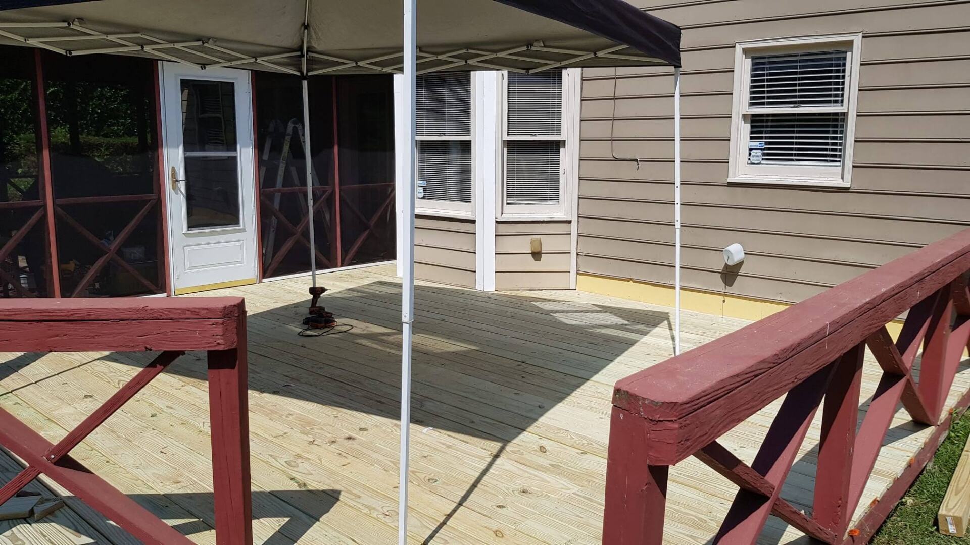 Wooden deck with red railings and a canopy next to a house with windows.