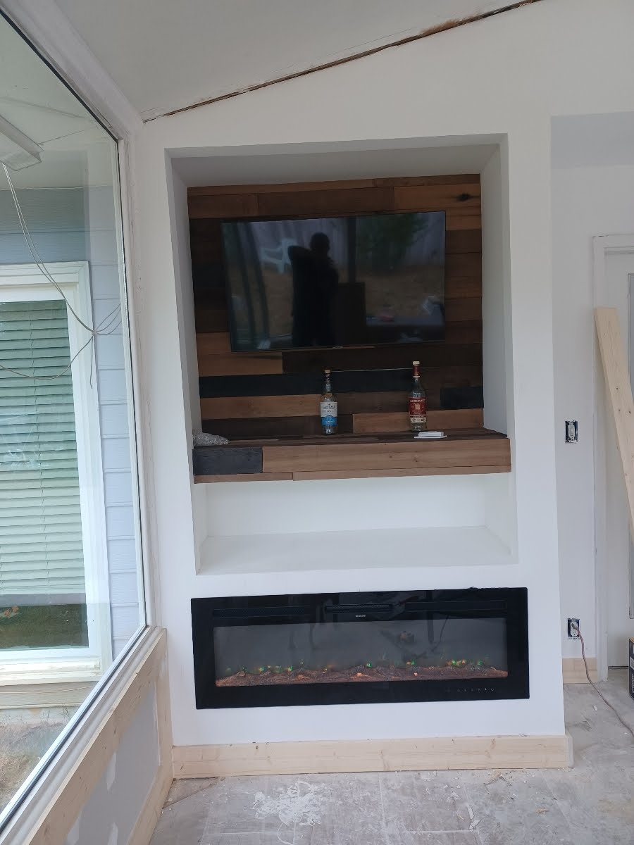 Built-in entertainment center with fireplace, TV, and shelves in a white-walled room, featuring wood paneling.