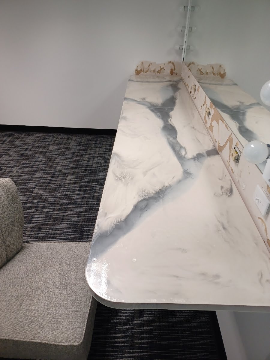 Epoxy resin table with blue-gray veining, under a chandelier, next to a gray fabric chair and black carpet.