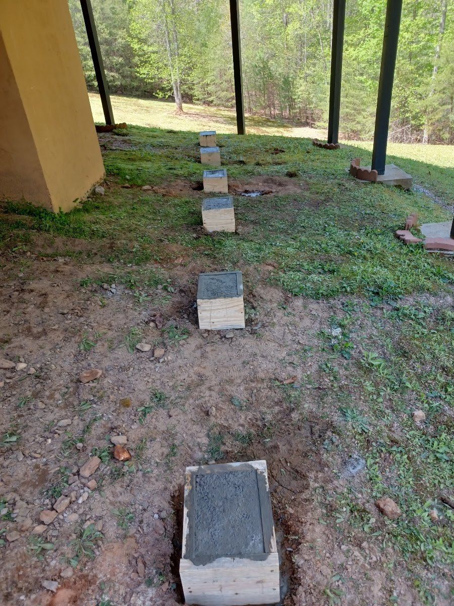 Wooden forms filled with wet concrete are set in the dirt path under a porch.