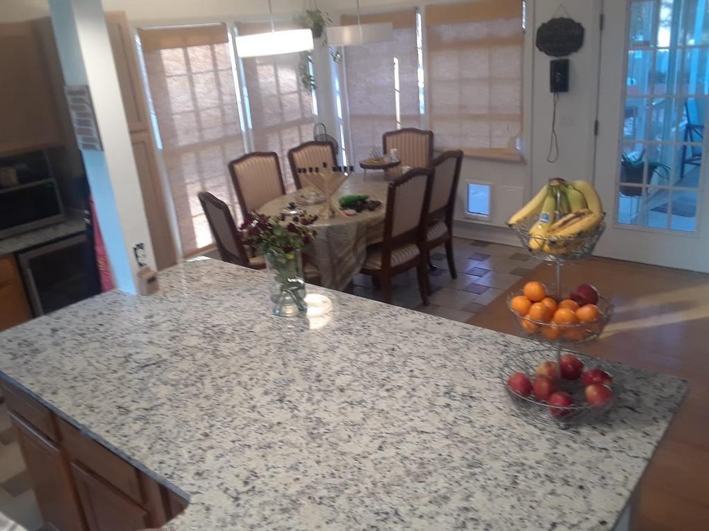 Kitchen with granite countertop, dining table set for guests, fruit bowl, and windows.