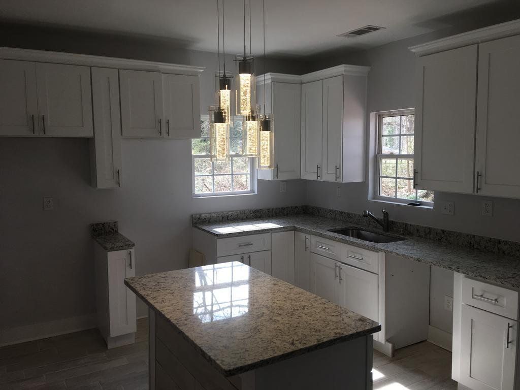 White kitchen with granite countertops and island, pendant lights over island.