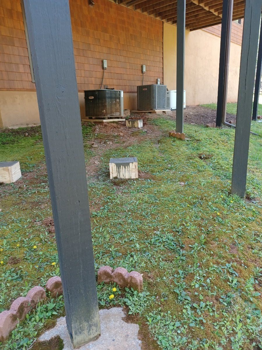 Exterior of a building with AC units on concrete blocks and grassy area with support columns.