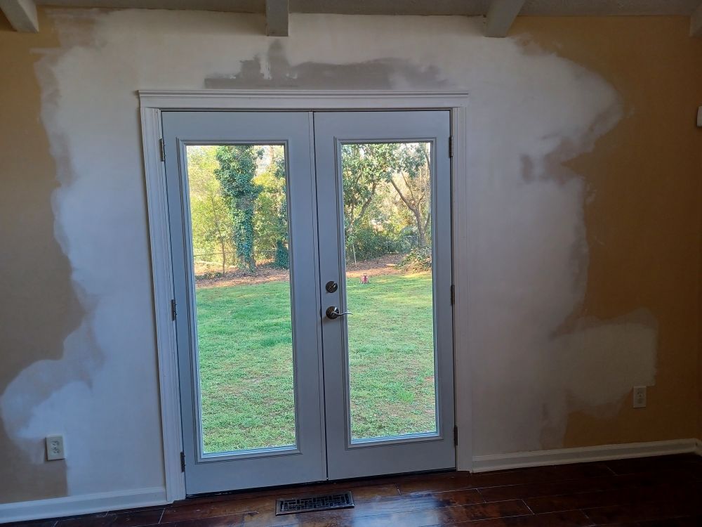 French doors with white trim and view of a yard, surrounded by walls with patched white paint.