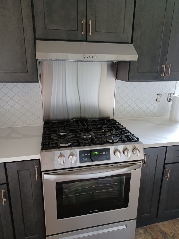 Kitchen with stainless steel range, vent hood, dark cabinets, white countertops and tiled backsplash.