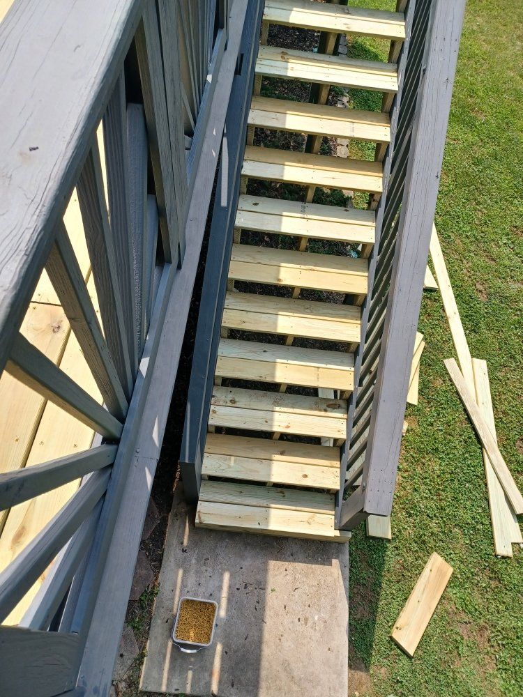 Wooden staircase leading from a deck to the ground, painted gray, with green grass in view.