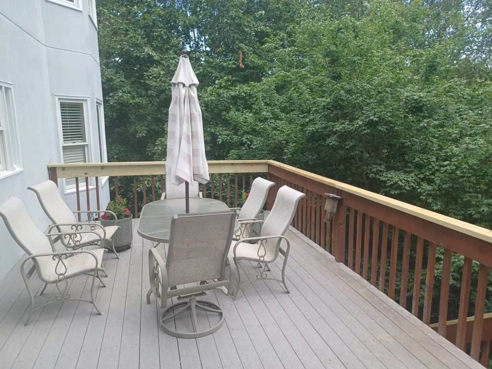 Deck with patio furniture: table, chairs, and umbrella.  Wooden railing and trees in background.