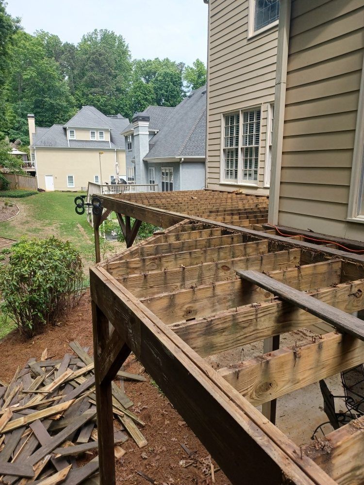 Deck under construction, wood frame exposed, brown with surrounding soil, adjacent to a beige house, residential setting.